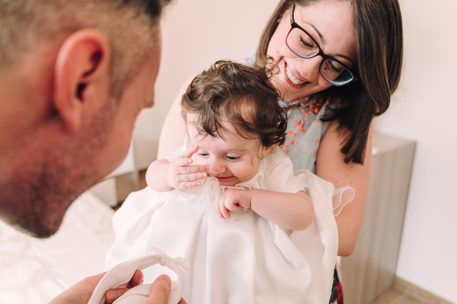 fotografo di battesimo. la fotografia rappresenta i due genitori con in braccio la loro bimba, durante la preparazione prima del battesimo.